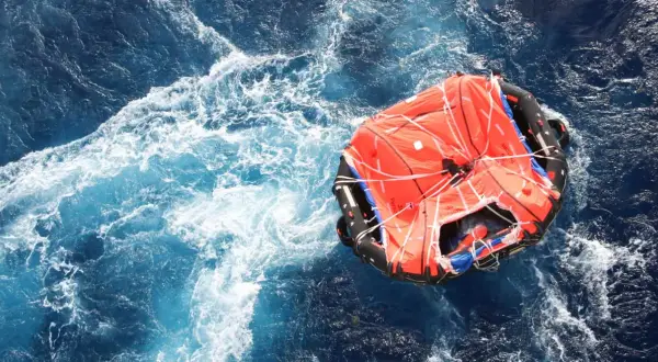 Una zattera di salvataggio arancione galleggia in un mare agitato. Il suo significato è speranza e sopravvivenza.