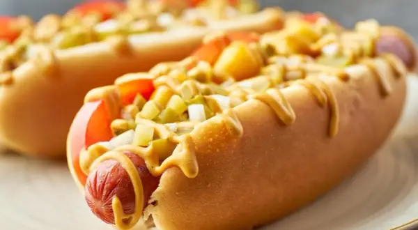 Dwa apetyczne hot dogi z Żabki, polane musztardą, z dodatkiem pomidorów i ogórków. Zastanawiasz się, ile kcal ma hot dog z Żabki?