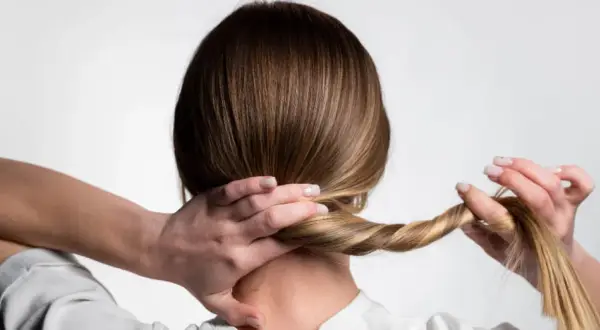 Manos trenzando el cabello rubio para crear peinados para dormir que mantengan el pelo bonito.