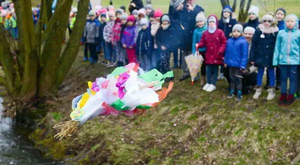 Dzieci obserwują topienie Marzanny, symboliczne pożegnanie zimy. Kolorowa kukła leci do wody.