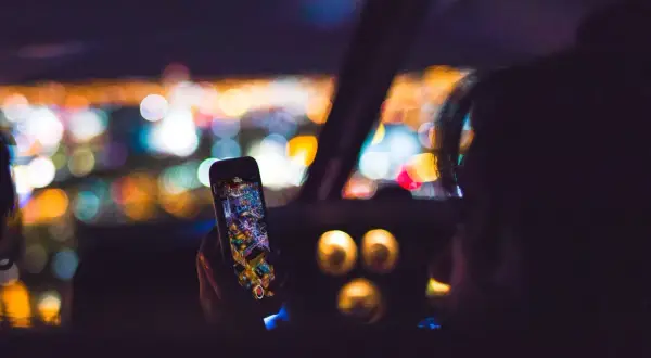Hand hält Handy mit Stadtansicht, während sie geblitzt wird. Bokeh-Lichter im Hintergrund.