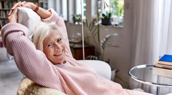 Vrolijke oudere vrouw ontspant in een fauteuil, genietend van rust. Een lat relatie elkaar weinig zien, maar ze vindt geluk in haar eigen gezelschap.
