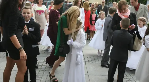 Dzieci w strojach komunijnych i dorośli na zewnątrz.