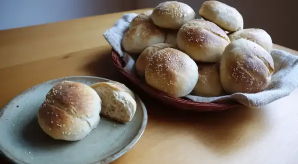 Färska frallor med sesamfrön, redo att avnjutas. En korg full av nybakade godsaker och en tallrik med en delad fralla. Perfekt för frukost eller fika.