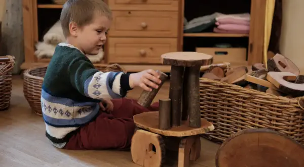 Ein Junge spielt mit Holzbausteinen, die das Waldorf Konzept widerspiegeln. Natürliche Materialien fördern Kreativität und Fantasie.