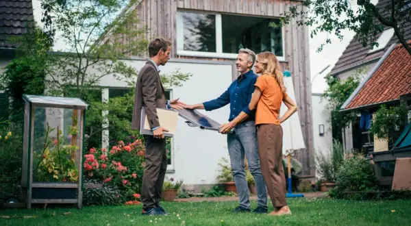 Beratung zu energetischer Sanierung Pflicht 2030: Ein Berater zeigt einem Paar ein Solarpanel im Garten vor ihrem Haus.