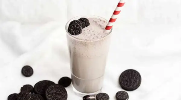 Batido cremoso de Oreo en un vaso con pajita a rayas, rodeado de galletas Oreo.