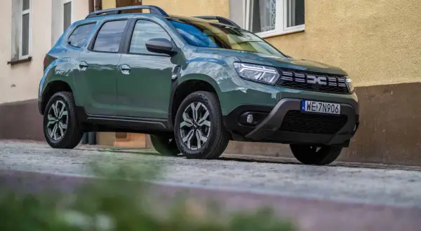 Zielony Dacia Duster na brukowanej ulicy. Wiele pozytywnych dacia duster opinie potwierdza jego wszechstronność.