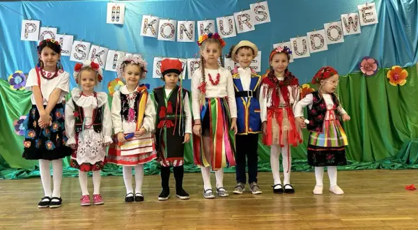 Dzieci w pięknych strojach ludowych prezentują się na scenie podczas konkursu.