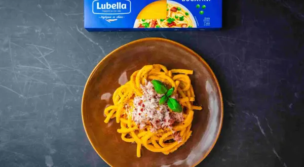 Talerz makaronu Bucatini Lubella posypany serem i ziołami, obok opakowanie makaronu.