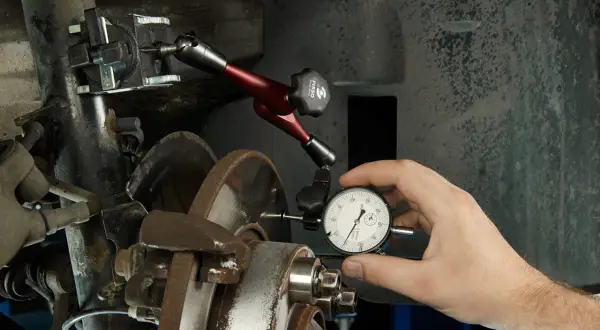 Mechanik mierzy bicie tarczy hamulcowej, by zdiagnozować drgania kierownicy podczas hamowania.
