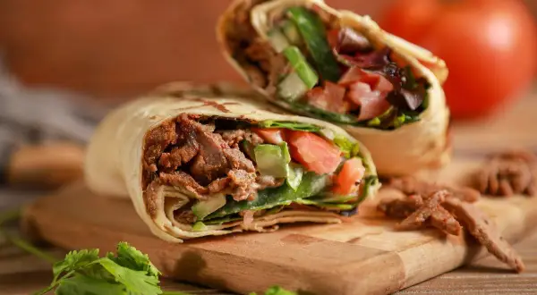 Kebab zawinięty w tortillę z mięsem, warzywami i ziołami na desce.