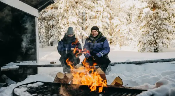 Couple réchauffé au feu de bois en Laponie. Idéal pour savoir quand partir en Laponie pour une expérience hivernale magique.