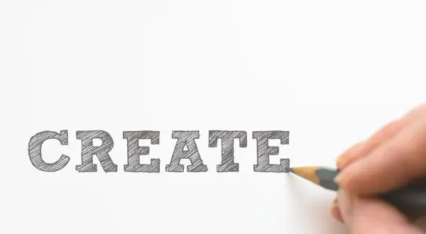 Un cartel curso con la palabra "CREATE" escrita a lápiz. Una mano dibuja la última letra, invitando a la creatividad.