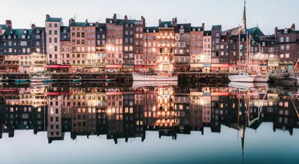 Les maisons colorées de Honfleur se reflètent dans l'eau calme, parfait pour un weekend. Bateaux amarrés, lumières douces.