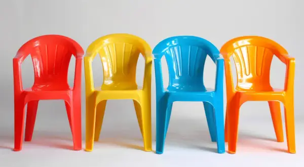 Cztery kolorowe plastikowe krzesełka: czerwone, żółte, niebieskie i pomarańczowe. Idealne do ogrodu, gdy zastanawiasz się, czym pomalować plastik.