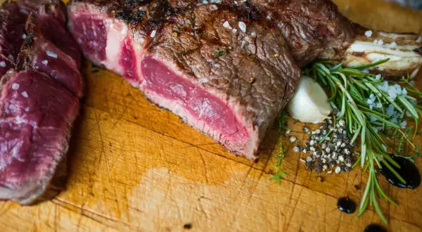 Une belle côte de bœuf saignante, assaisonnée de gros sel et de poivre, avec du romarin et de l'ail sur une planche en bois.