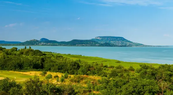 Malowniczy krajobraz z jeziorem Balaton na Węgrzech, zielone wzgórza i błękitne niebo.