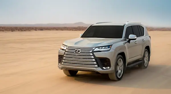 Srebrny Lexus LX 600 przemierza pustynię, unosząc tumany piasku.