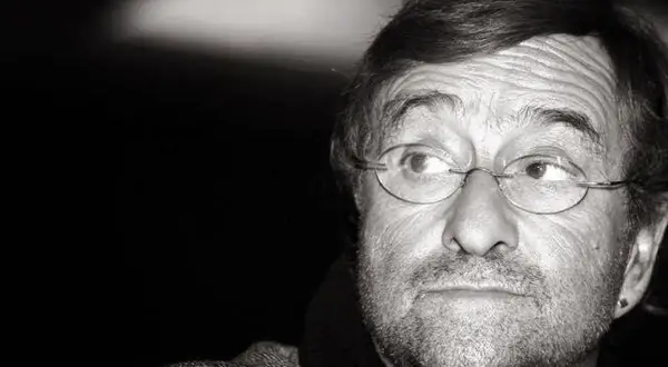 Ritratto in bianco e nero di un uomo con occhiali rotondi, barba e un'espressione pensierosa. Il suo sguardo è rivolto di lato, come se stesse ascoltando attentamente il **caruso testo**.