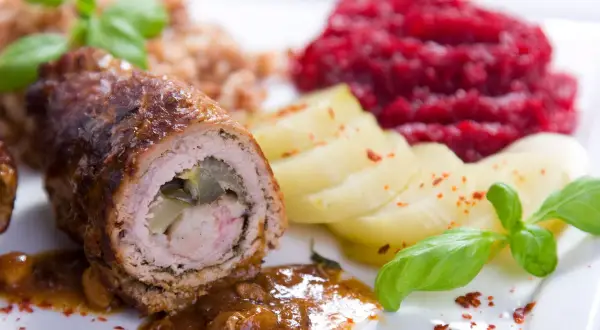Roladki wołowe z ogórkiem, ziemniakami, kaszą i buraczkami na białym talerzu.