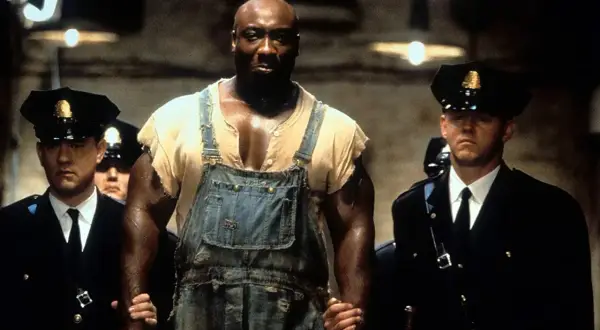 John Coffey w ogrodniczkach, prowadzony przez strażników więziennych. Scena z filmu "Zielona mila 2".
