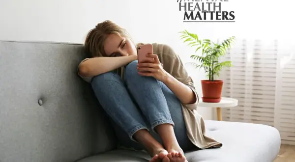 Junge Frau sitzt allein auf Sofa, depressiv weil single. Sie hält ihr Handy, #MENTAL HEALTH MATTERS.