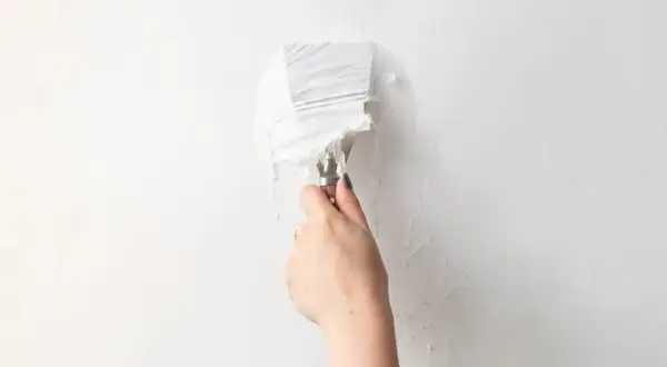 Mano con spatola che rimuove carta da parati bianca da un muro.