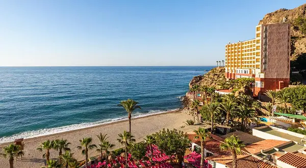 Hotel con piscina y tumbonas rosas junto a la playa de aguadulce roquetas de mar, con el mar azul de fondo.