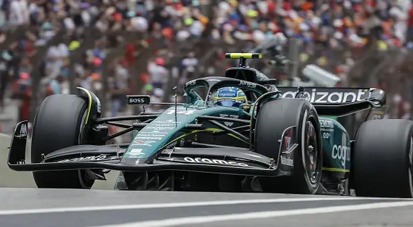 Coche de Fórmula 1 verde y negro en pista, con público al fondo. El piloto, con casco azul, busca ser libres 2.