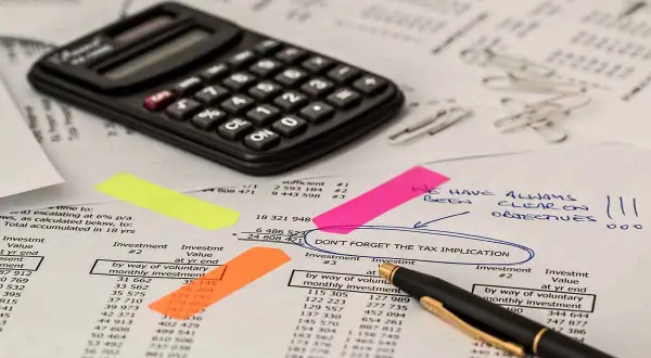 Kalkulator i dokumenty finansowe. Na jednym z nich zaznaczono "DON'T FORGET THE TAX IMPLICATION", co może dotyczyć np. podatek od gruntów rolnych poniżej 1 ha.