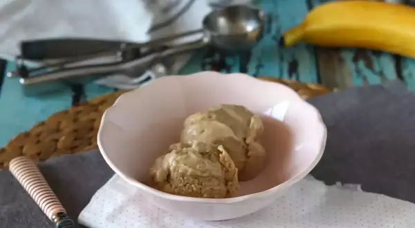 Två skopor krämig bananglass i en rosa skål. En banan ligger i bakgrunden, perfekt för ett enkelt bananglass recept.