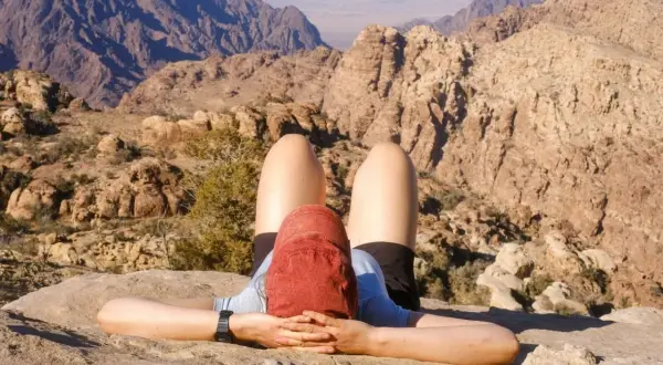 Une personne se repose sur un rocher, les mains derrière la tête, admirant le paysage désertique lors d'un trek en Jordanie.