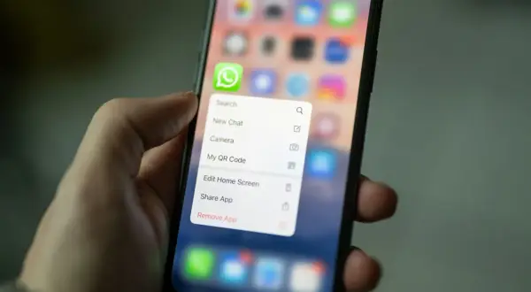 Dłoń trzyma smartfon z menu aplikacji WhatsApp. Można tu znaleźć opcję "Kopia zapasowa WhatsApp" (choć nie jest widoczna na ekranie, jest to kontekst).