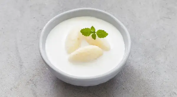 Kogel-mogel czy jest zdrowy? Miseczka z deserem z bitej śmietany, kawałkami banana i listkiem mięty.