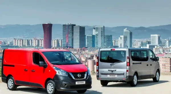 Dwa samochody dostawcze Nissan NV300, czerwony i srebrny, stoją na tle panoramy miasta z nowoczesnymi budynkami.