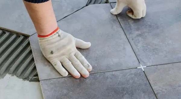 Pose de carrelage avec double encollage. Mains gantées ajustant une dalle sur un lit de mortier frais.