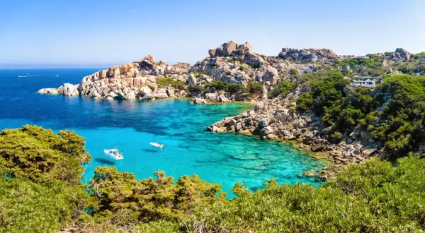 Türkisblaues Meer, Felsenbuchten und grüne Macchia – diese Szenerie verspricht die beste Reisezeit Sardinien. Kleine Boote schaukeln im Wasser.