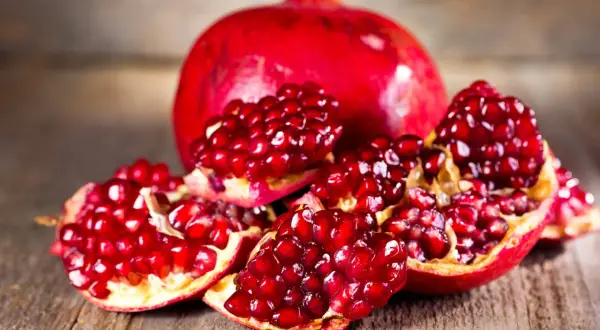 Saftige Granatapfelkerne auf Holz. Die Frucht, woher kommt der Granatapfel, stammt ursprünglich aus Persien und dem Nahen Osten.