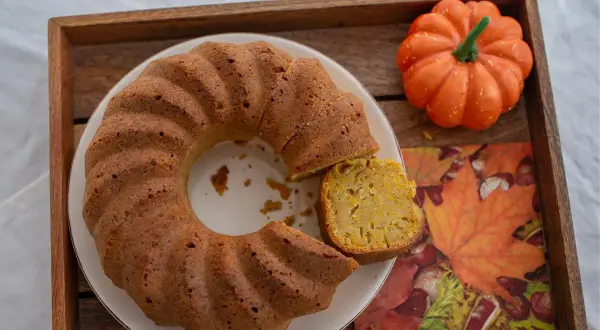 Un delicioso bizcocho de calabaza, con una porción cortada, sobre una bandeja de madera junto a una calabaza decorativa y una servilleta de hojas de otoño.