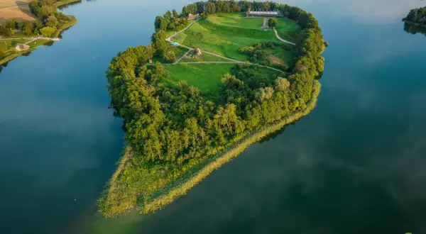 Wielkopolskie miasto koło Kalisza, Ostrowo Lednickie, z wyspą na jeziorze, porośniętą drzewami i trawą, z zabudowaniami.