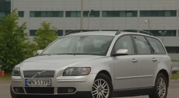 Srebrne Volvo V50 kombi zaparkowane przed nowoczesnym budynkiem.