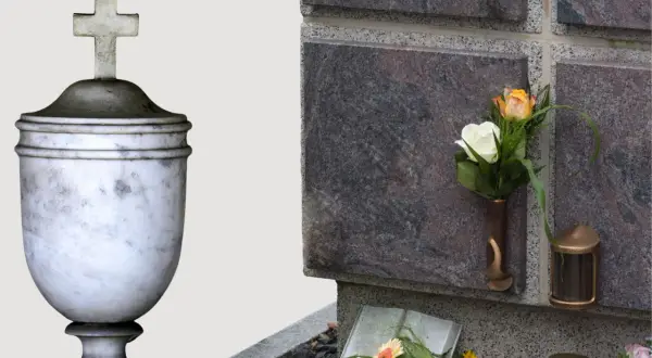 Kamienna urna z krzyżem i kwiaty przy ścianie kolumbarium.