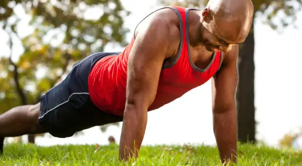 Homme chauve en tenue de sport faisant un exercice bras sur l'herbe.