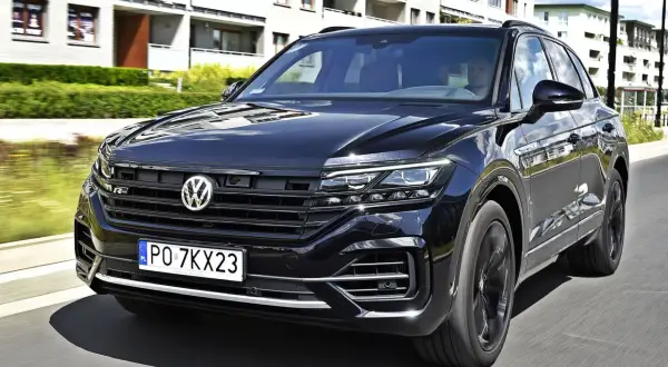 Czarny VW Touareg 3.0 TDI z polskimi tablicami PO 7KX23 jedzie ulicą obok nowoczesnych budynków.