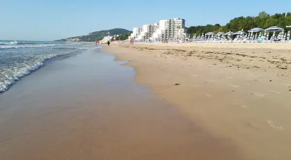 Piękna plaża w Albena Bułgaria. Fale obmywają piaszczysty brzeg, a w oddali widać hotele i rzędy parasoli.