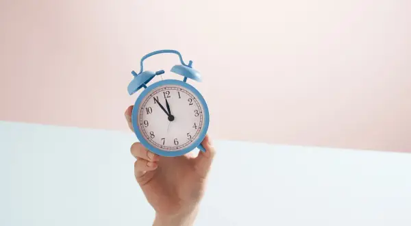 En hand håller en blå väckarklocka. Snart är det dags för antagningsbesked gymnasiet!