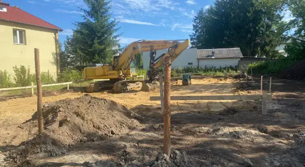 Plac budowy, gdzie koparka przygotowuje działkę budowlaną pod fundamenty.