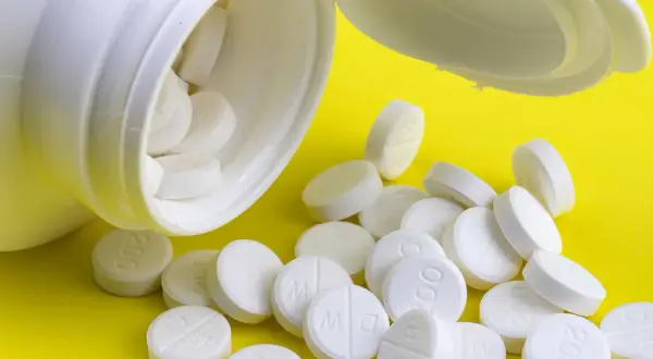 En vit burk med tabletter som kan vara adhd medicin för barn. Tabletterna ligger utspridda på en gul bakgrund.