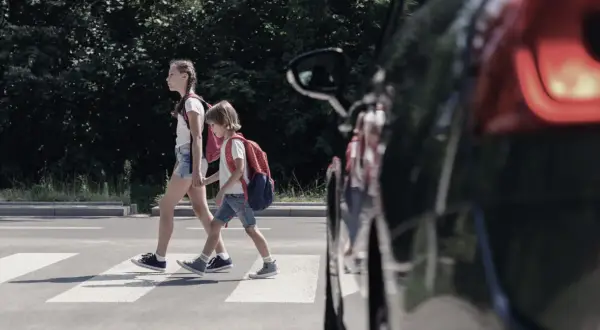 Dwoje dzieci, pieszy na pasach, z plecakami przechodzi przez ulicę.